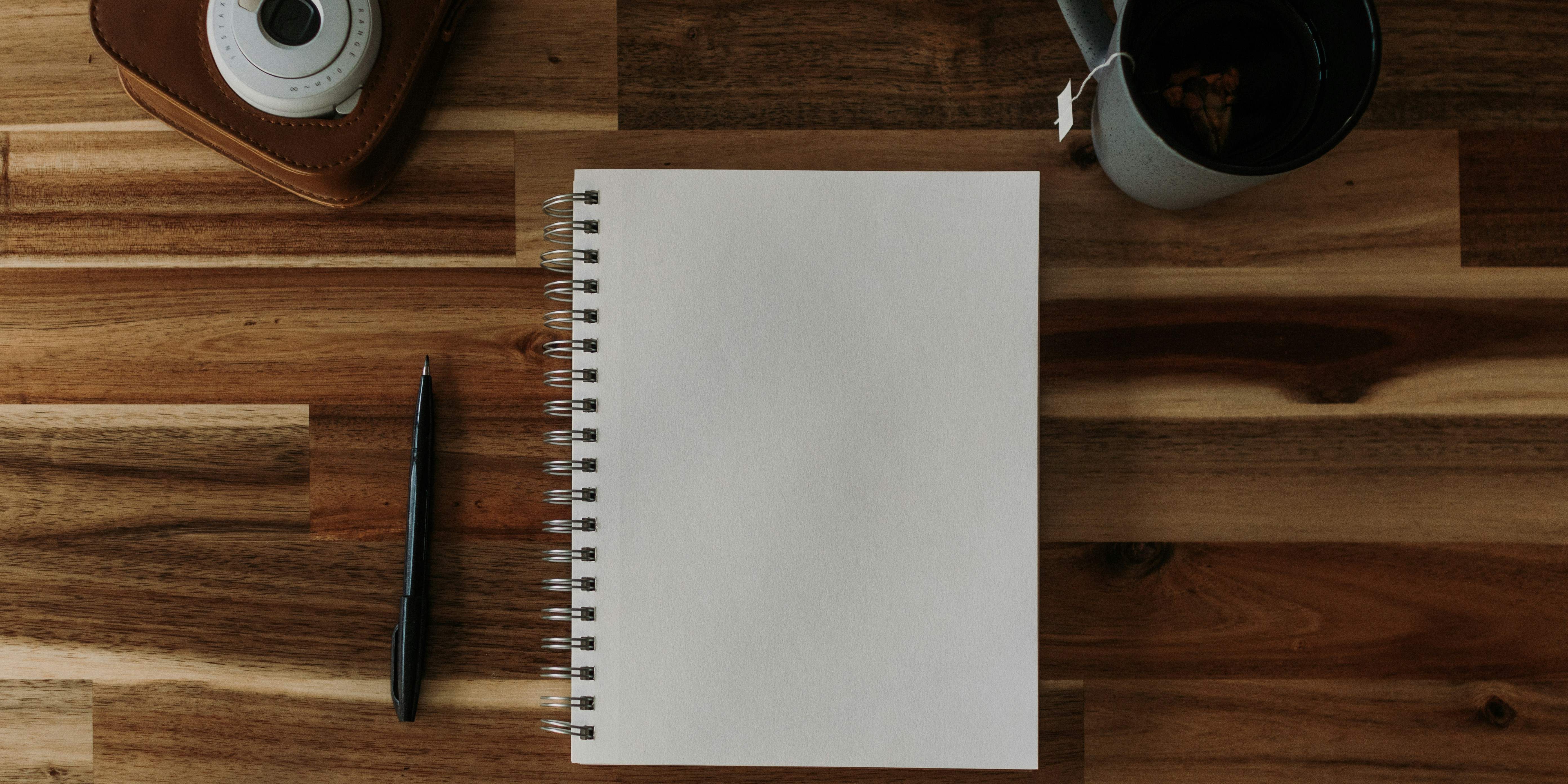 A discovery conversation — notebook, coffee and a laptop on a warm wooden desk